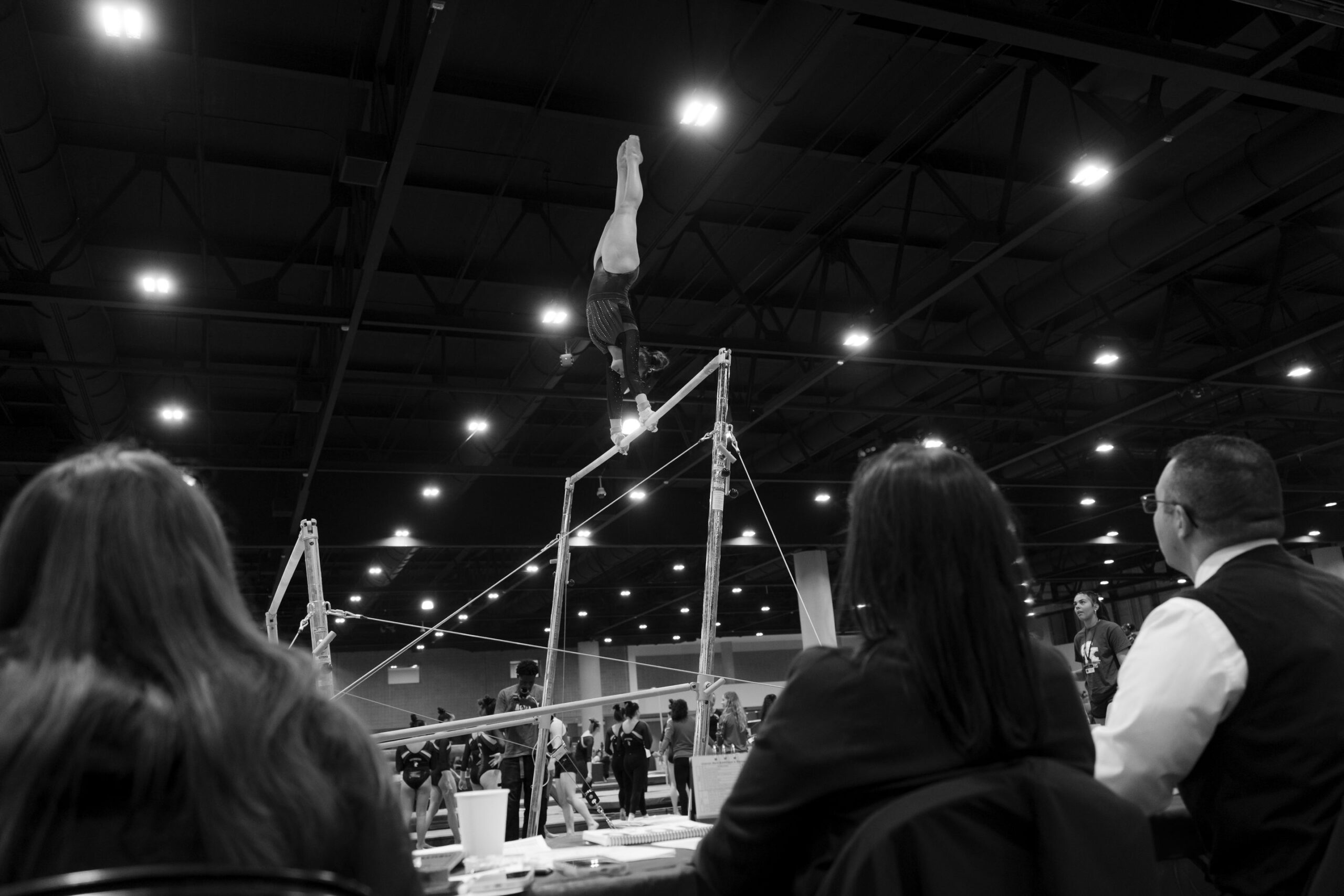A judge follows an uneven bars routine from the side of the podium at UCG Nationals