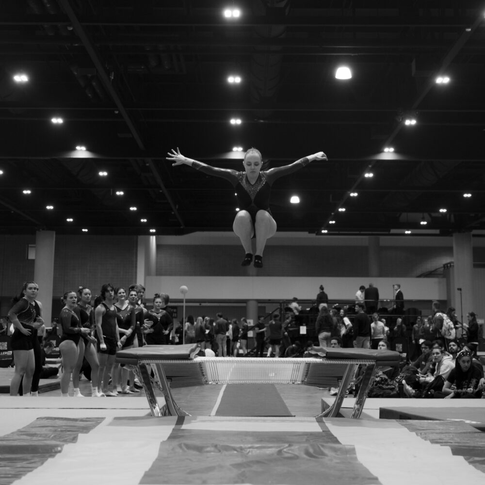 An athlete flies above the trampoline while the community watches at UCG Nationals