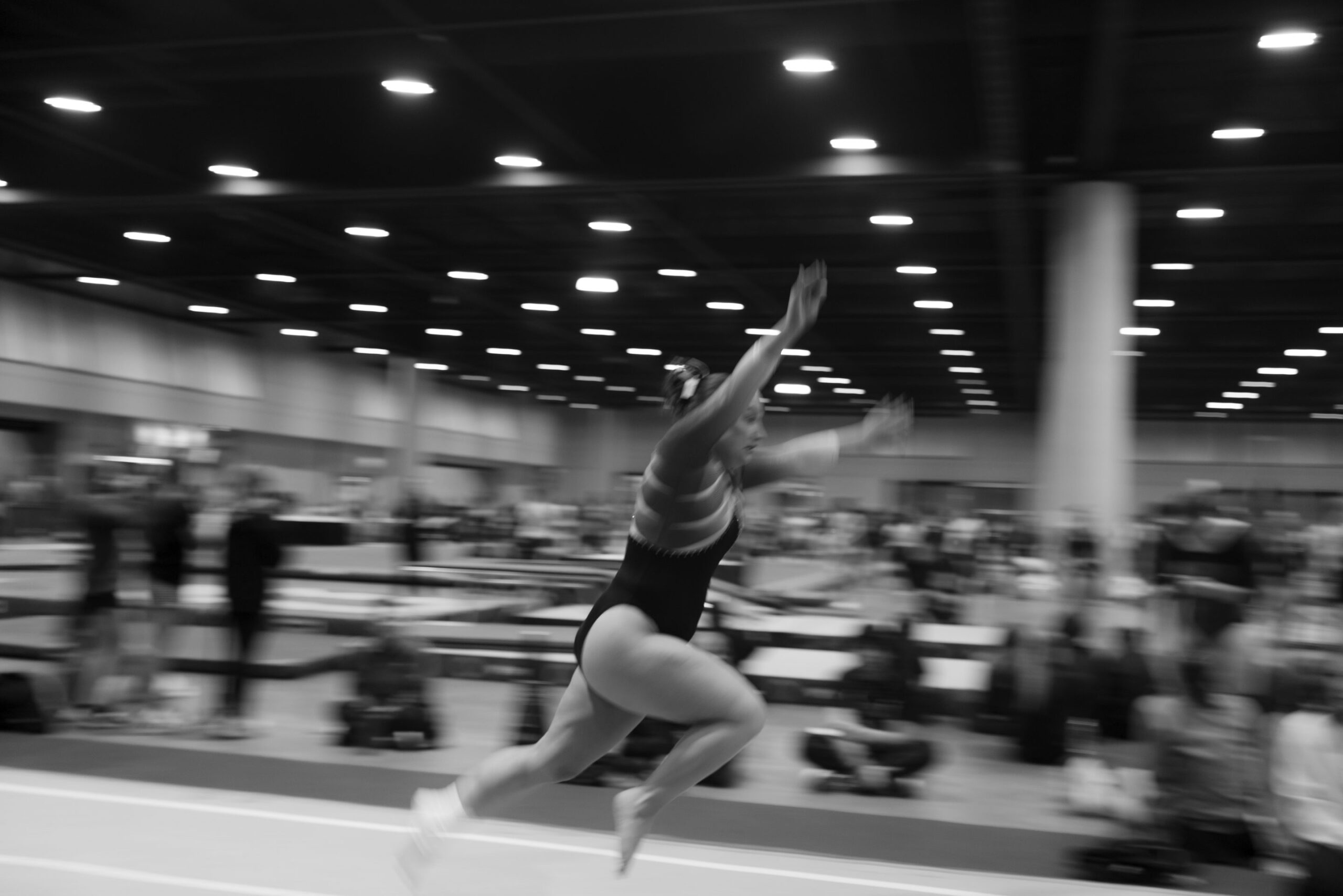 A gymnast sprints into a tumbling pass, the hall blurred behind her, at UCG Nationals